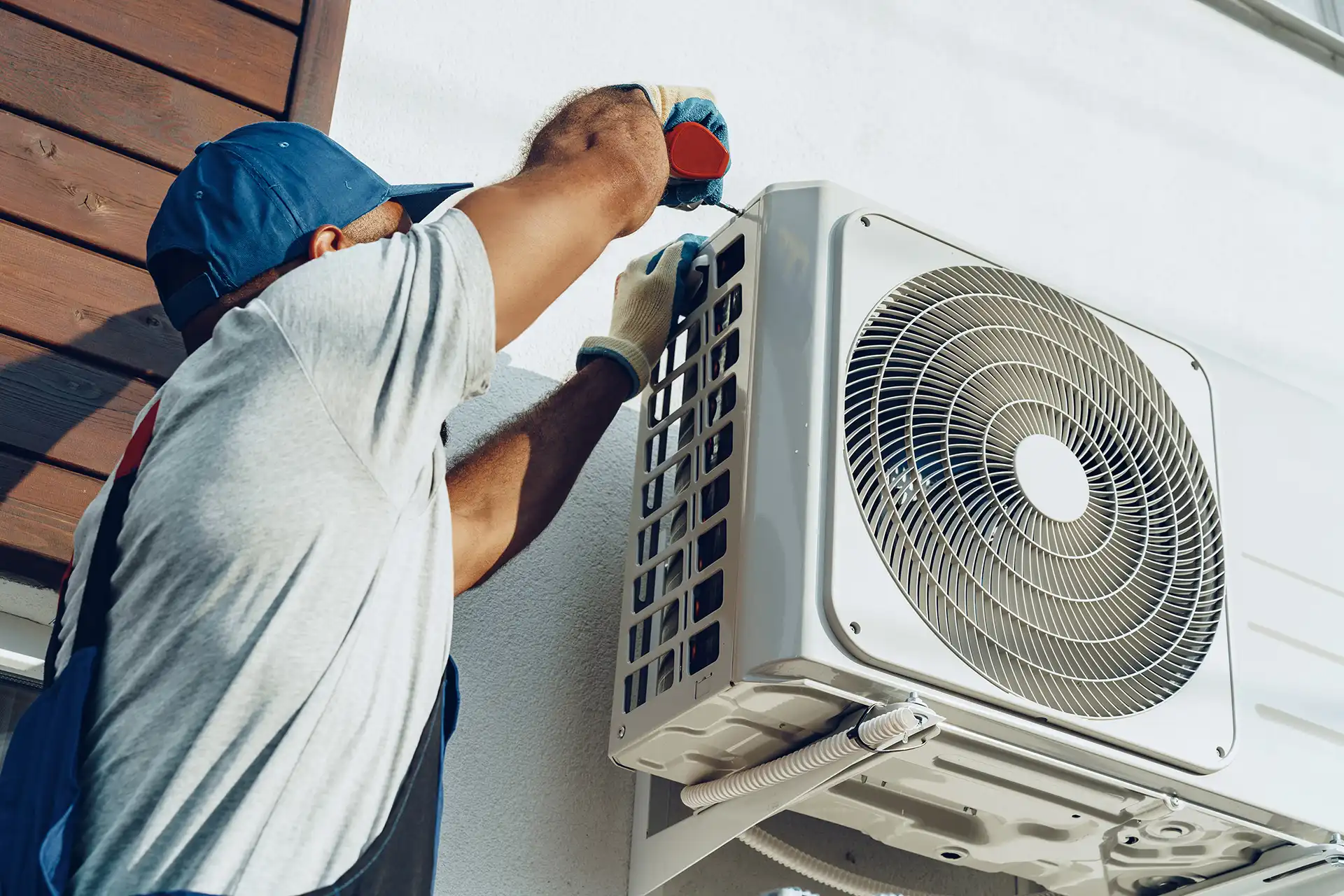 Technician installing an outdoor mini-split air handler unit on an exterior wall