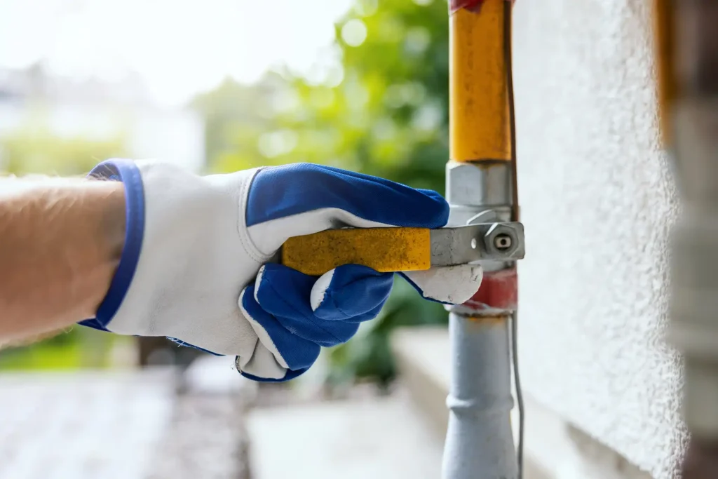 Technician in work gloves turning an exterior gas shutoff valve on a home's gas line