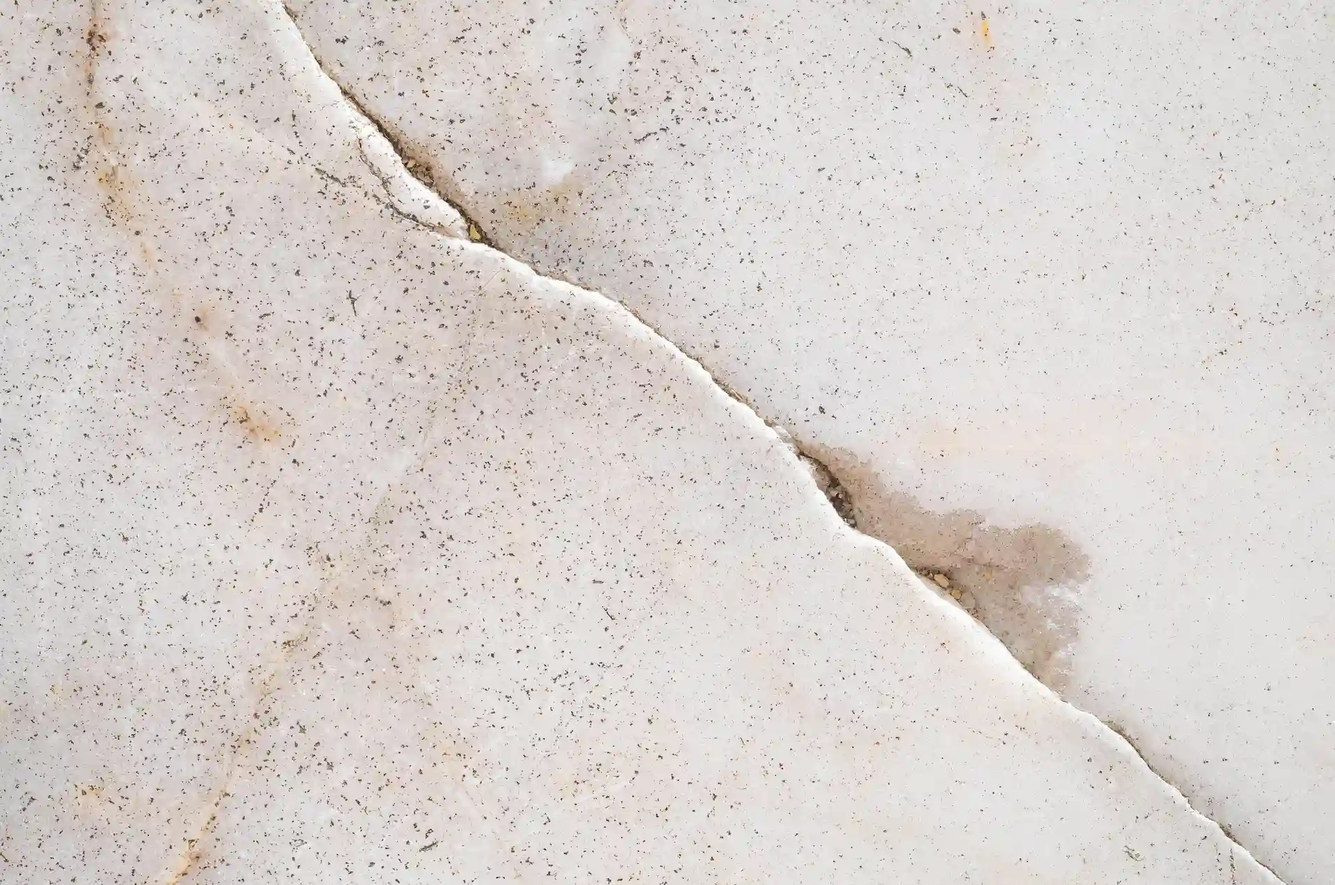 Close-up of a cracked concrete or stone slab surface with a visible fracture line and moisture staining.