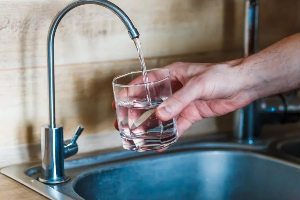 Hand filling a glass with water from a kitchen faucet-mounted filtration spout.