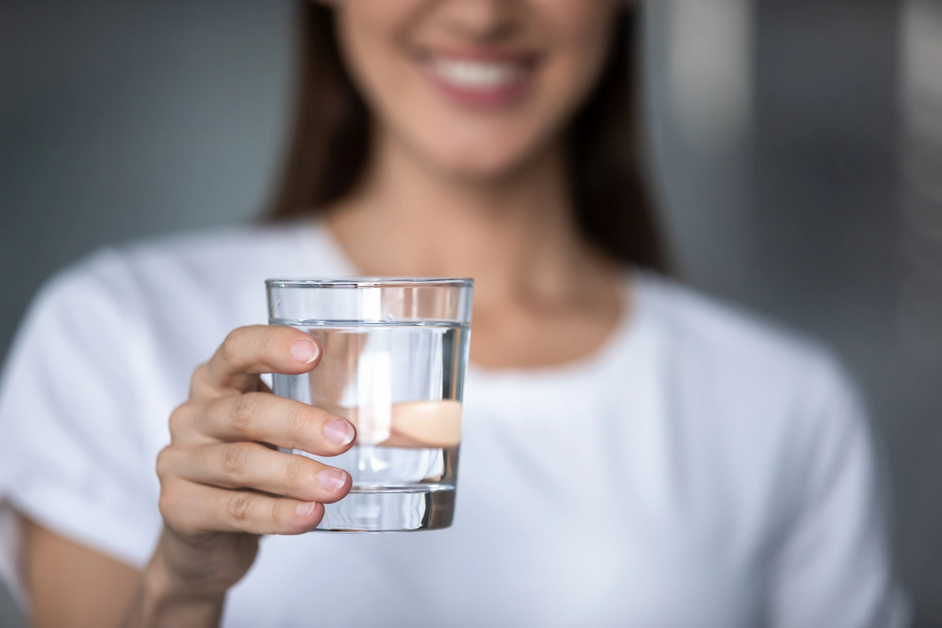 Close-up of a smiling woman holding a glass of clear drinking water.